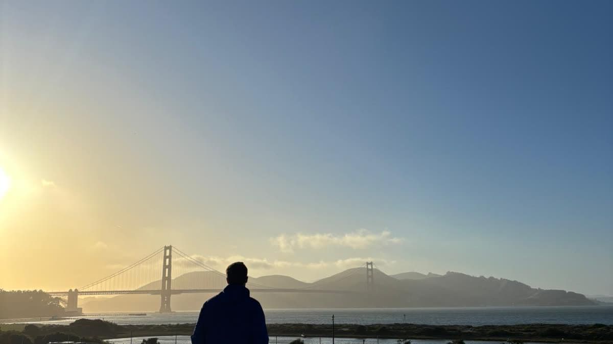 A person standing alone at dawn looking across the water toward the Golden Gate Bridge