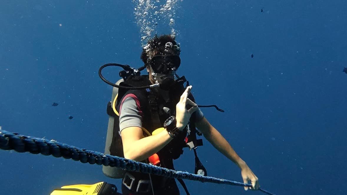 A scuba diver descending a guide line into deep blue open water