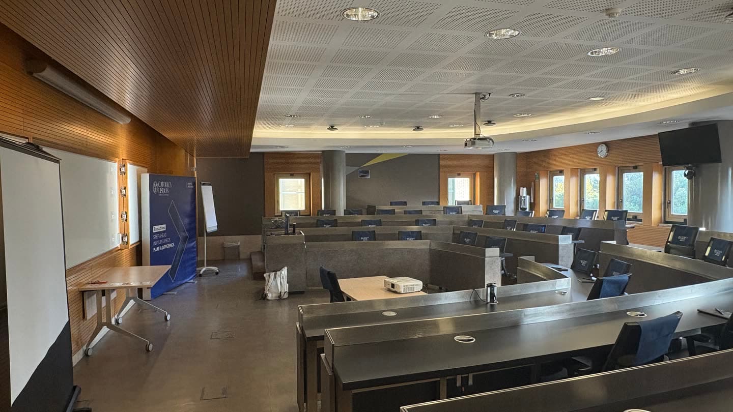 An empty university seminar room with tiered desks facing a blank projector screen