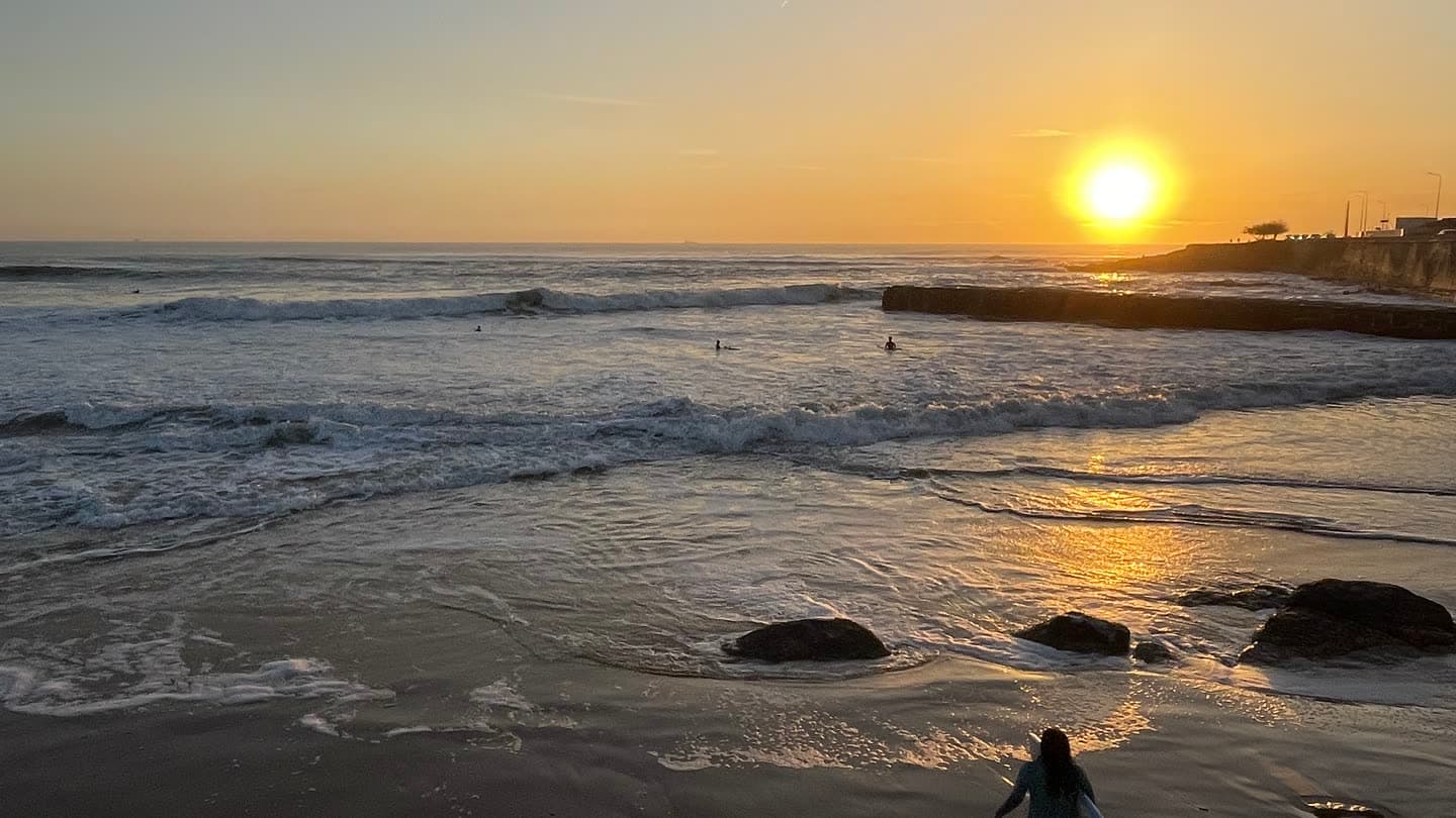 Waves breaking on a beach at sunset with a breakwater in the distance
