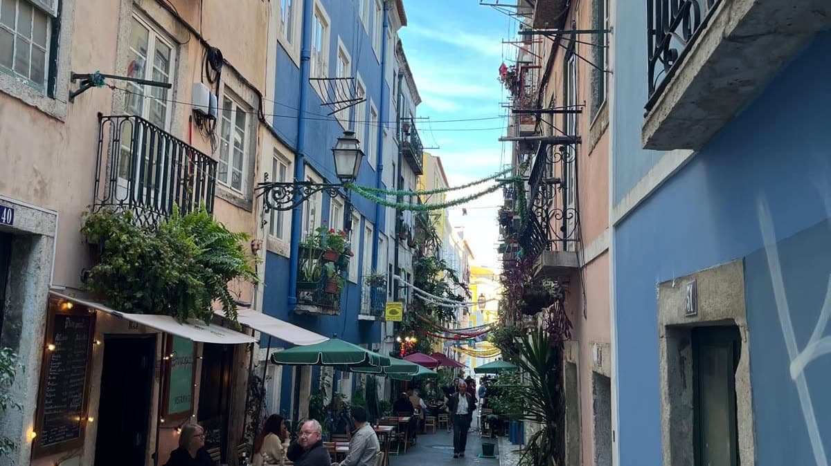 A narrow Lisbon street lined with cafés and tiled buildings in late afternoon light