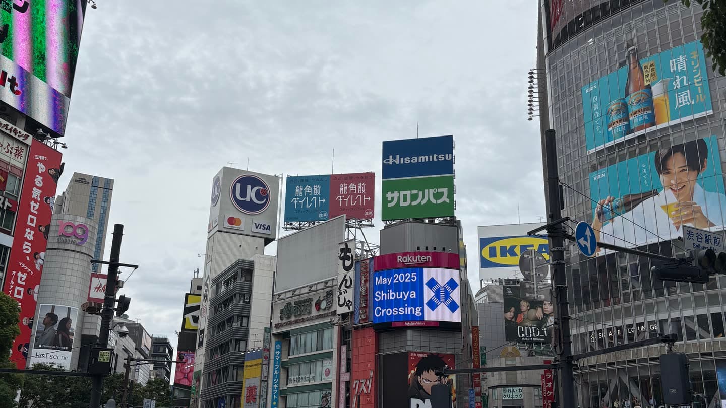 A crowded street crossing in Shibuya, Tokyo, under dense overhead signage