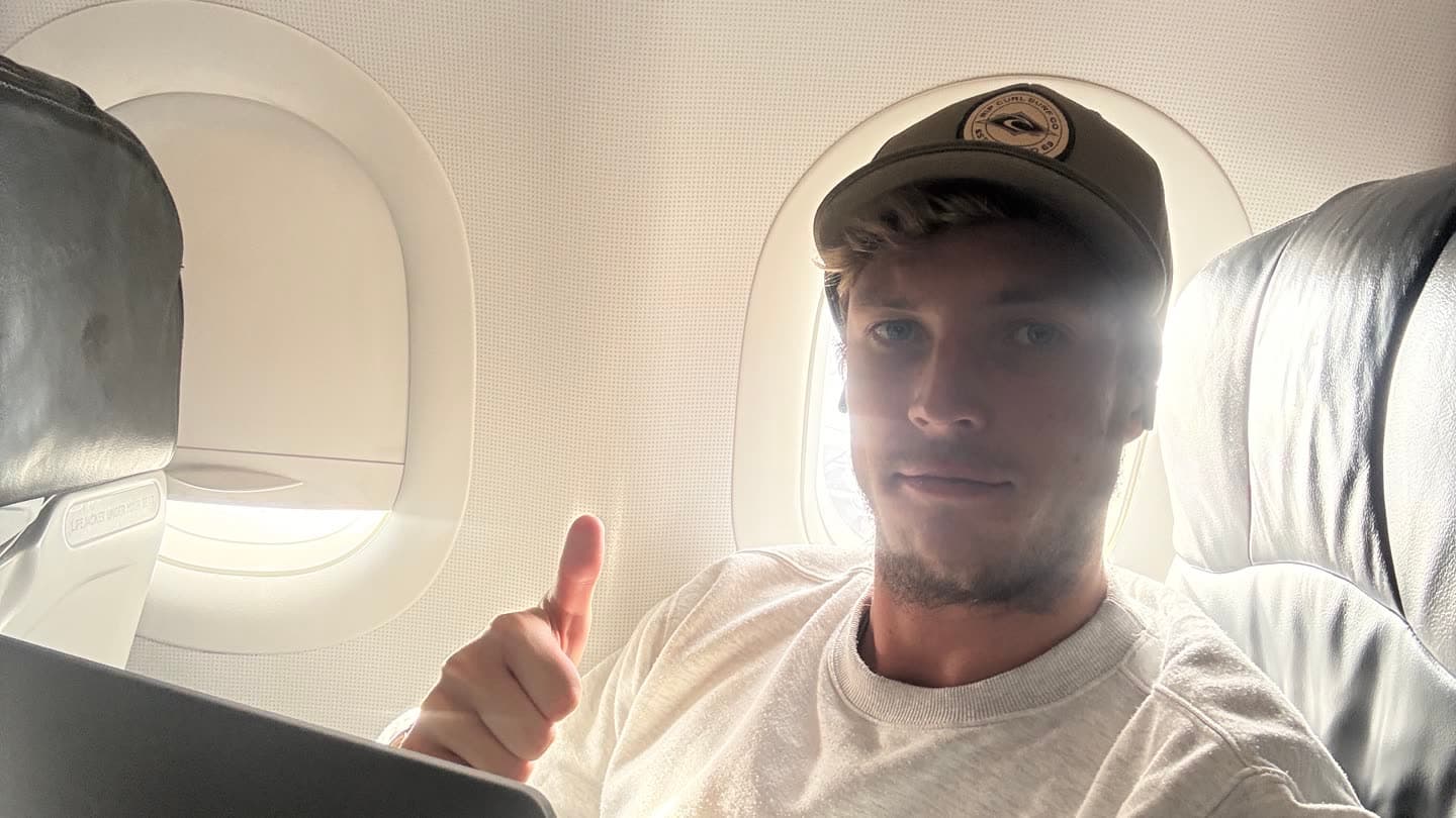 Marco working on a laptop in an aeroplane seat, tray table down, cabin lights dimmed