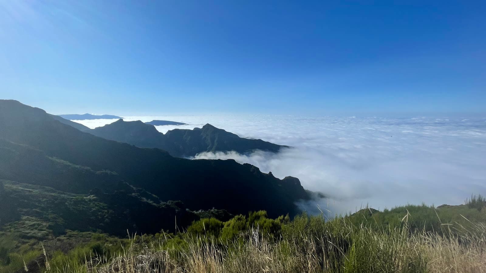 A mountain ridge in Madeira rising above a solid layer of cloud, with clear sky beyond it
