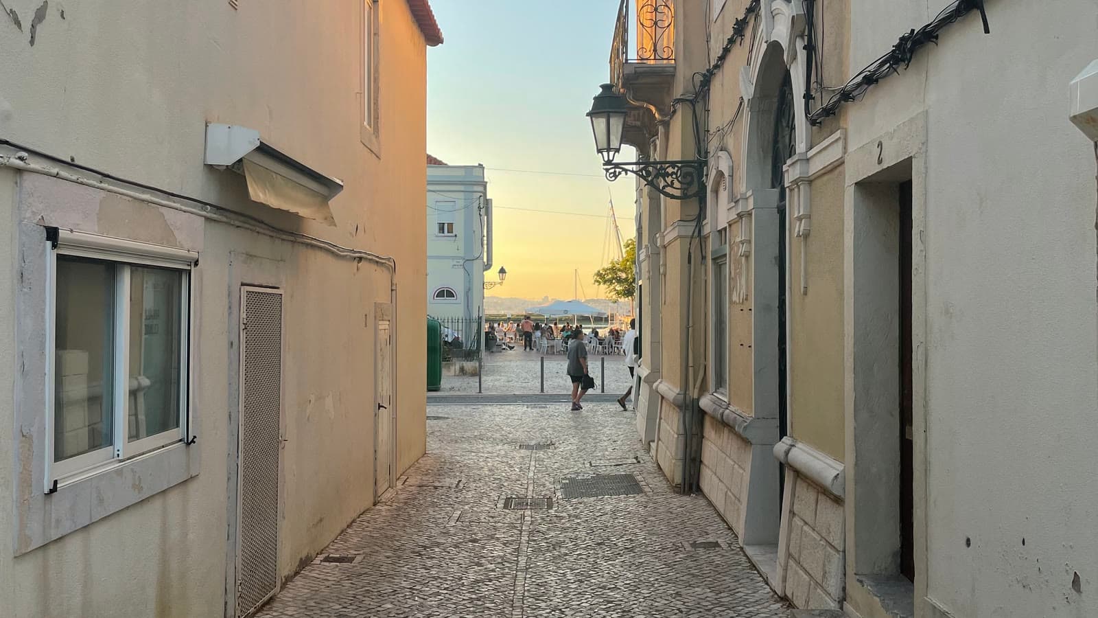 A quiet cobbled side street in Almada opening onto the Tejo waterfront across from Lisbon