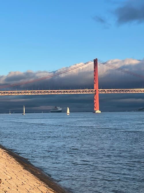 View across the Tejo river in Lisbon, sailboats passing under the Ponte 25 de Abril